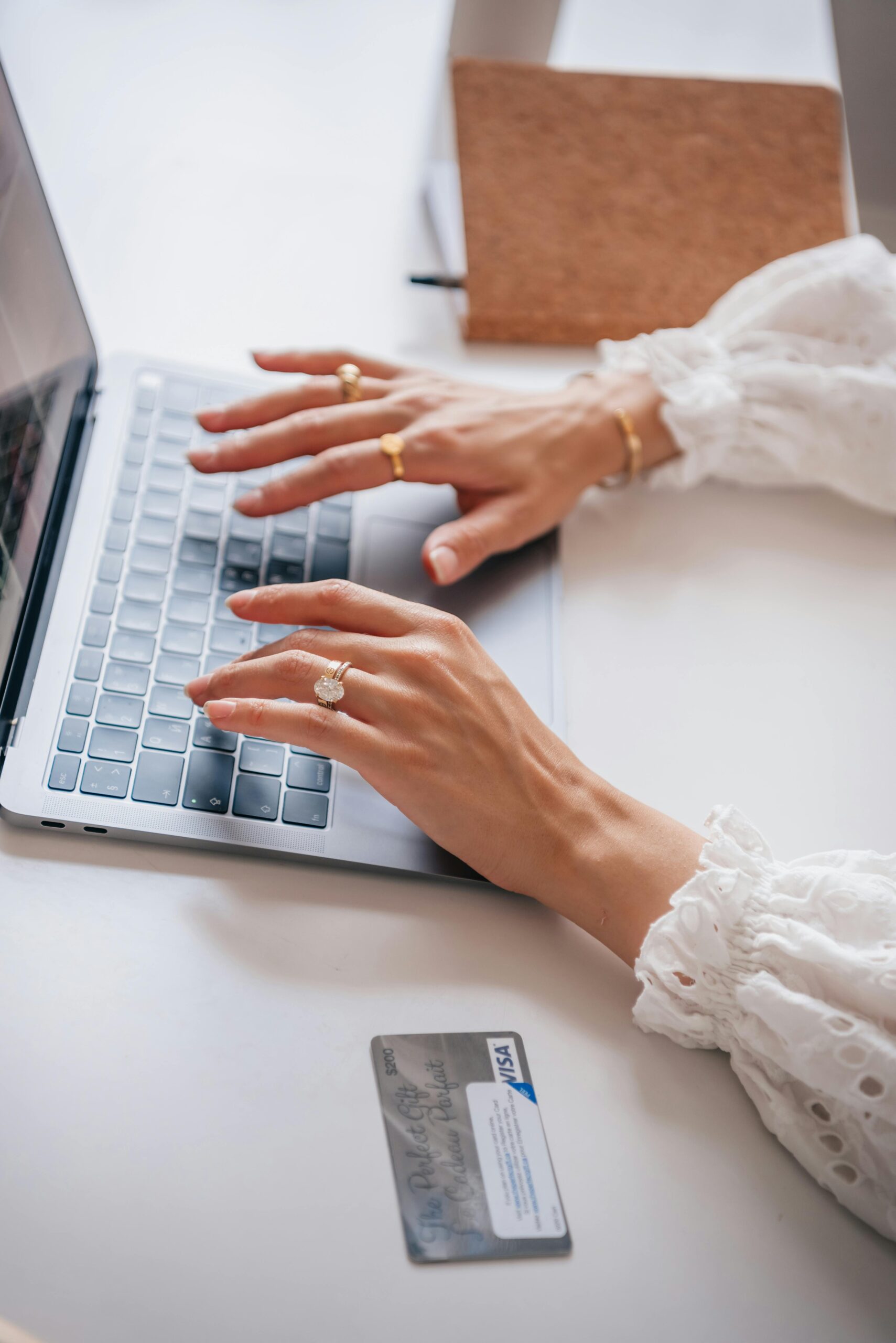 A woman with elegant rings types on a laptop next to a credit card, illustrating online shopping.